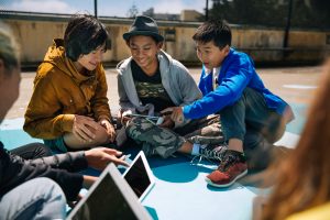  children on the ground on a playground gathered around a tablet reading