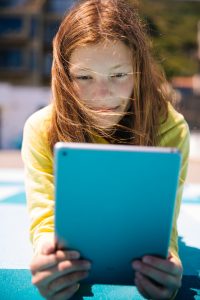  children on the ground on a playground gathered around a tablet reading