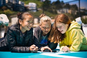  children on the ground on a playground gathered around a tablet reading